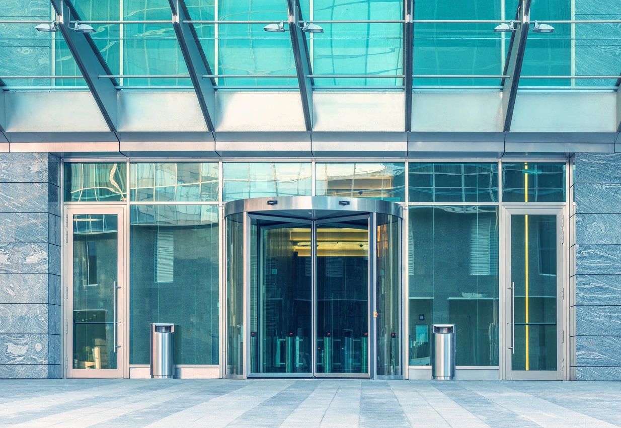 A large glass building with two doors and a sidewalk.